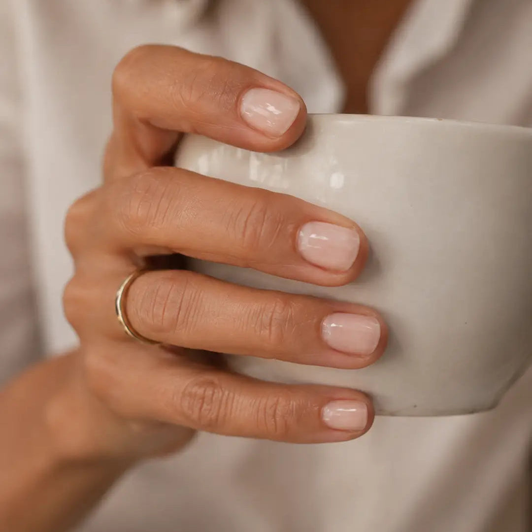 Main tenant une tasse, ongles nude brillants protégés par le soin Nara Glow 23Beauty Paris